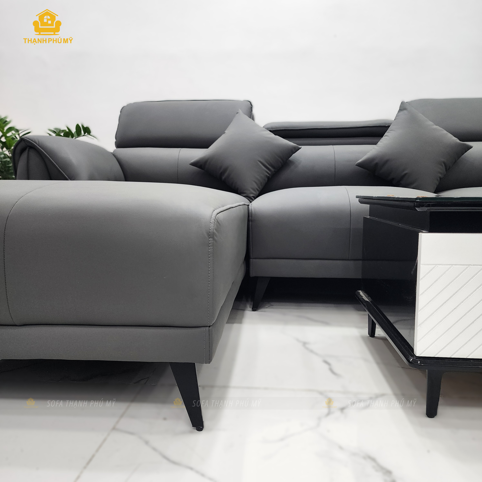 Góc nghỉ và chân sắt cao màu đen của sofa góc L da simili xám, cạnh bàn trà mặt kính đen trắng – Sofa Thạnh Phú Mỹ