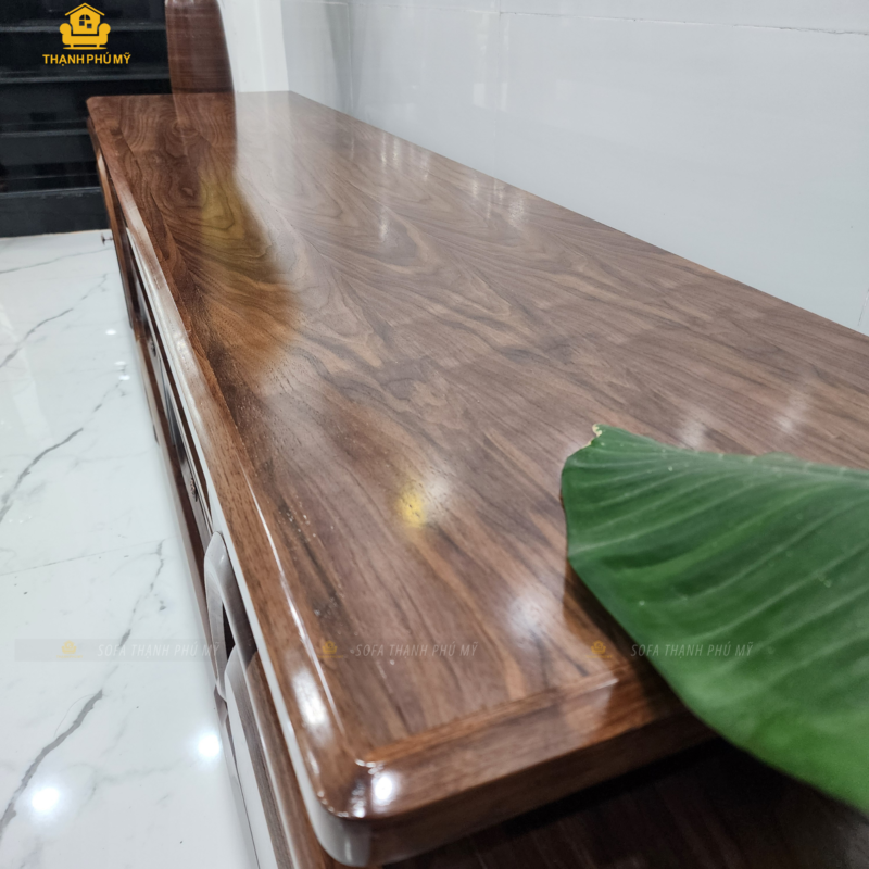 Bề mặt mặt kệ tivi gỗ Óc Chó tự nhiên được chà nhám kỹ và phủ PU bóng nhẹ, hiển thị rõ đường vân gỗ và sắc nâu socola trầm tại không gian Nội Thất Thạnh Phú Mỹ.